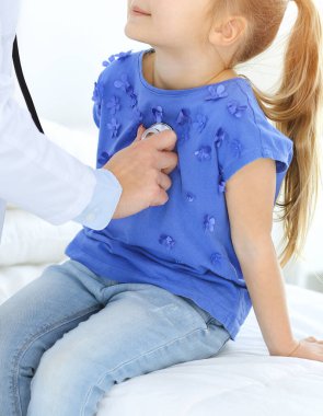 Doktor steteskopla küçük bir kızı muayene ediyor. Her zamanki tıbbi muayenede gülümseyen çocuk hasta. Tıp ve sağlık hizmetleri kavramları