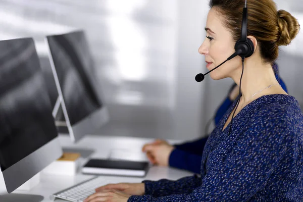 Deux femmes d'affaires ont des conversations avec les clients par écouteurs, tout en étant assis au bureau dans un bureau moderne. Groupe de personnes diverses dans un centre d'appels. Télémarketing et service à la clientèle — Photo