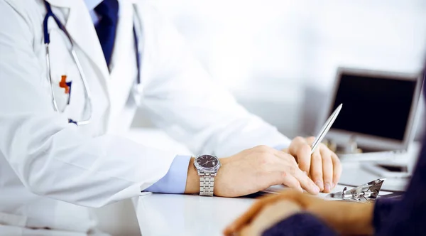 Paciente joven desconocida discute los resultados de sus pruebas médicas con un médico, mientras está sentada en el escritorio de un consultorio del hospital. Médico que usa portapapeles para llenar los registros del historial de medicamentos — Foto de Stock