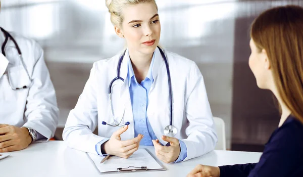 Жінка-лікар з колегою-чоловіком консультує пацієнтку, сидячи за столом у сучасній клініці. Ідеальна медична служба, концепція медицини — стокове фото