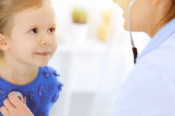 Arzt untersucht ein kleines Mädchen per Stethoskop. Glücklich lächelnder Kinderpatient bei der üblichen ärztlichen Untersuchung. Medizin- und Gesundheitskonzepte — Stockfoto