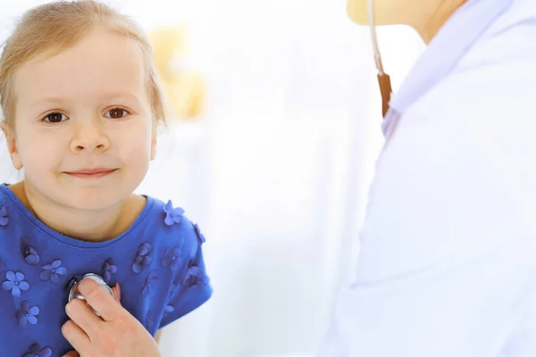 Arzt untersucht ein kleines Mädchen per Stethoskop. Glücklich lächelnder Kinderpatient bei der üblichen ärztlichen Untersuchung. Medizin- und Gesundheitskonzepte — Stockfoto