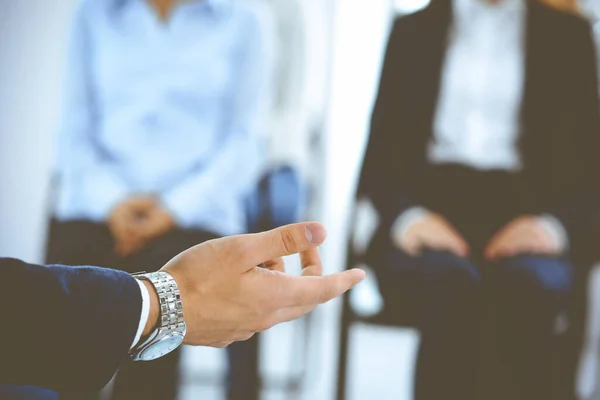 Business man making presentation to group of people, close-up. Speaker delivering a seminar to his colleagues or business training in office. Teamwork and coaching concept