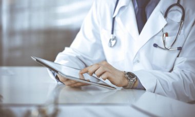 Bilinmeyen erkek doktor klinikteki tablet bilgisayarla yakın planda çalışıyor. İşteki genç doktor. Mükemmel sağlık hizmeti, tıp konsepti