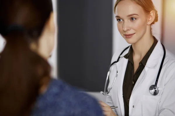 Alegre sorridente feminino médico e paciente mulher discutindo exame de saúde atual enquanto sentado na clínica ensolarada. Serviço médico perfeito no hospital. Conceito de medicina — Fotografia de Stock