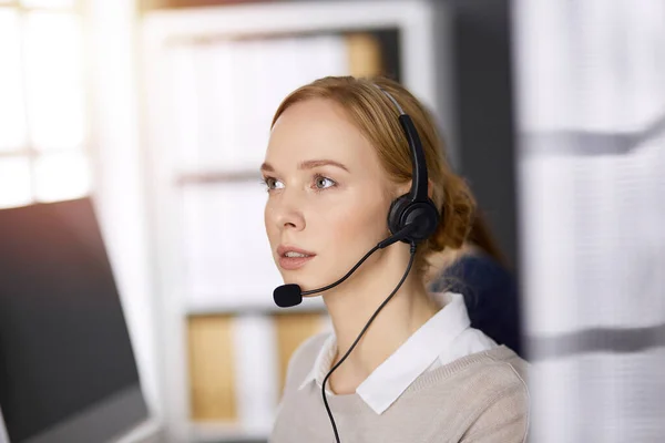 Femme d'affaires parlant par casque tout en étant assis dans un bureau ensoleillé. Centre d'appels et divers groupes de personnes en affaires — Photo