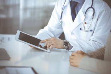 Bilinmeyen erkek doktor ve hasta kadın klinikte oturup tablet bilgisayar kullanırken bir şeyler tartışıyorlar. Hastanedeki en iyi sağlık hizmeti, ilaç, salgın durdurma.