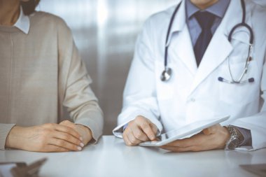 Bilinmeyen erkek doktor ve hasta kadın klinikte oturup tablet bilgisayar kullanırken bir şeyler tartışıyorlar. Hastanedeki en iyi sağlık hizmeti, ilaç, salgın durdurma.