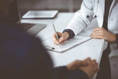 Bilinmeyen kadın-doktor, bir klinikteki dolapta birlikte otururken hastasına bazı tıbbi tavsiyeler yazıyor. Hekim bir dosya kullanıyor, yakın plan. Mükemmel.