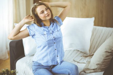 Mutlu sarışın kadın ellerini başının arkasına koyuyor koltuğa yaslanmış beyaz kadın tembelce hafta sonunun ya da rahat oturma odasında tatilin tadını çıkarıyor ev hanımı rahatlıyor ev işlerini başarıyla yapıyor.