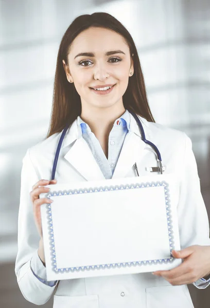 Glückliche junge Ärztin hält ein Zertifikat in den Händen. Berufsarzt bei der Arbeit in einer Klinik. Medizinkonzept — Stockfoto