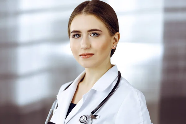 Amigável médico feminino de pé e segurando prancheta na clínica moderna. Retrato de médico sorridente alegre — Fotografia de Stock