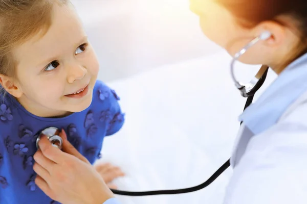 Doctor examinando a una niña por estetoscopio. Feliz niño sonriente paciente en la inspección médica habitual. Medicina y conceptos sanitarios —  Fotos de Stock