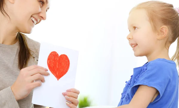 Mothers day concept. Child daughter congratulates mom and gives her postcard with red heart shape. Mum and girl happy smiling and hugging. Family fun and holiday — Stock Photo, Image