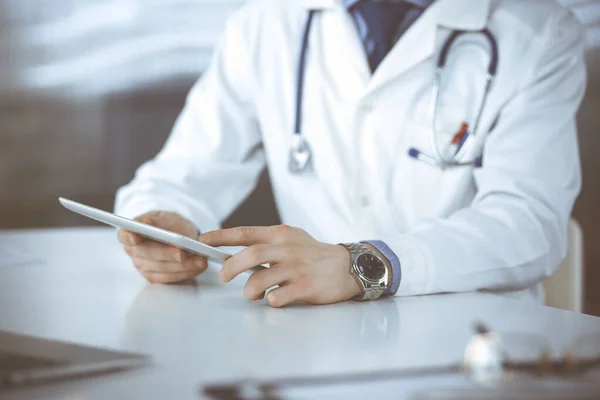 Médico masculino desconocido sentado y trabajando con Tablet PC en la clínica en su lugar de trabajo, primer plano. Médico joven en el trabajo. Servicio médico perfecto, concepto de medicina — Foto de Stock