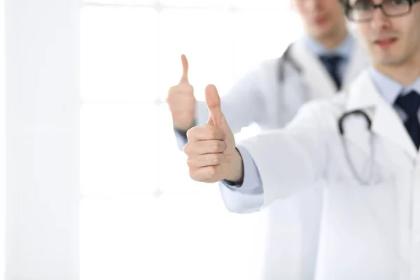 Two male doctors standing as a team and showing thumbs up as a symbol of the best service for patients in the clinic. Medicine and health care — Stock Photo, Image