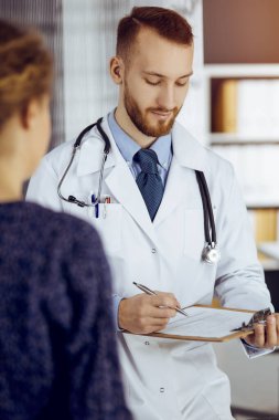 Dost canlısı sakallı doktor ve hasta kadın güneşli klinikte otururken sağlık muayenesini tartışıyorlar. Tıp konsepti