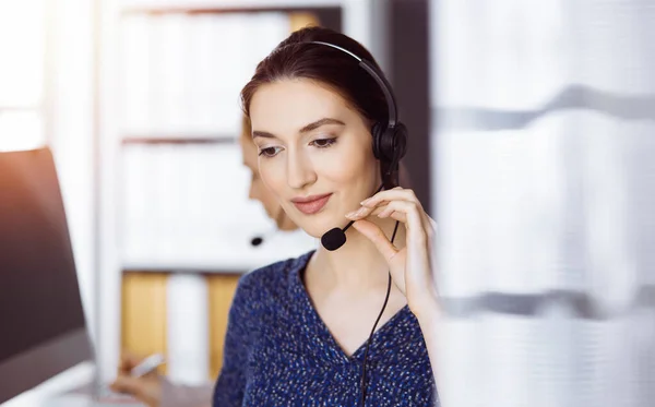 Latin american businesswoman talking by headset in office. Call center and diverse people group in business