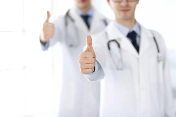 Dos médicos varones de pie como un equipo y mostrando los pulgares hacia arriba como un símbolo del mejor servicio para los pacientes en la clínica. Medicina y asistencia sanitaria —  Fotos de Stock