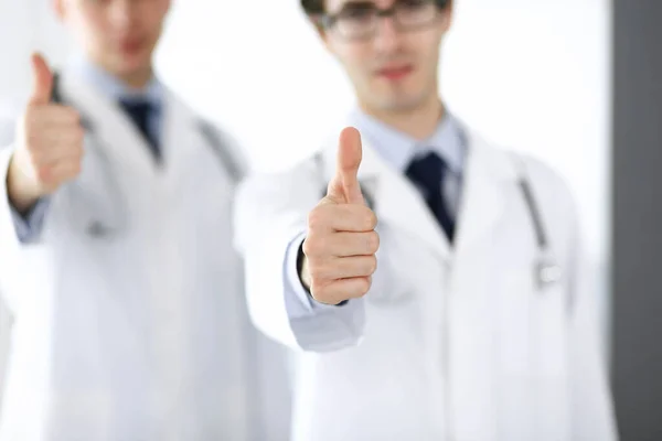 Dois médicos do sexo masculino em pé como uma equipe e mostrando os polegares para cima como um símbolo do melhor serviço para os pacientes na clínica. Medicina e cuidados de saúde — Fotografia de Stock
