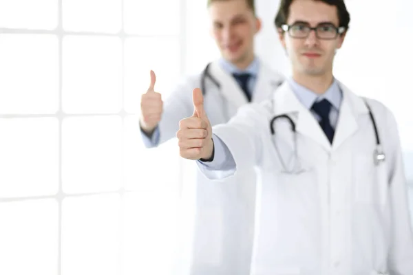 Zwei männliche Ärzte stehen als Team und zeigen Daumen nach oben als Symbol für den besten Service für Patienten in der Klinik. Medizin und Gesundheitsfürsorge — Stockfoto