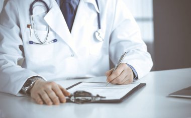 Bilinmeyen erkek doktor, klinikte, yakın planda pano ile oturuyor ve çalışıyor. İşteki genç doktor. Mükemmel sağlık hizmeti, tıp konsepti
