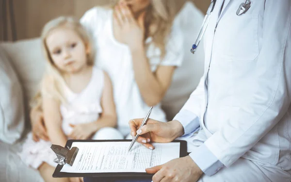 Doctor y paciente. Pediatra usando portapapeles mientras examina a la niña con su madre en casa. Niña enferma e infeliz en el examen médico. Concepto de medicina — Foto de Stock