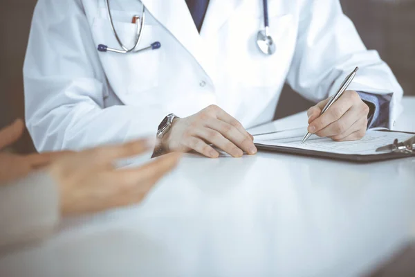 Hombre desconocido médico y mujer paciente discutiendo algo mientras está sentado en la clínica y el uso de portapapeles. El mejor servicio médico en hospital, medicina, parada pandémica — Foto de Stock