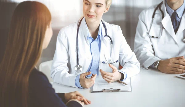 Mulher-médico com colega do sexo masculino estão consultando mulher paciente enquanto sentado na mesa na clínica moderna. Serviço médico perfeito, conceito de medicina — Fotografia de Stock