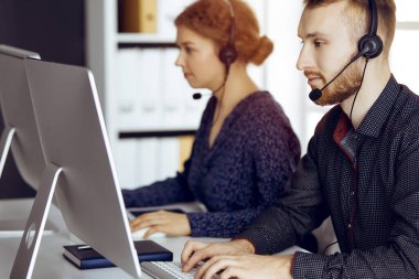 Modern güneşli ofiste otururken kulaklıkla konuşan sakallı iş adamı. Çağrı merkezinde çeşitli insanlar grubu