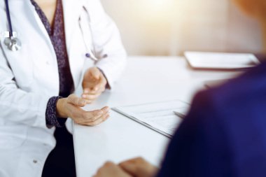 Tanımlanamayan kadın-doktor, bir klinikteki güneşli dolapta birlikte otururken hastasıyla teşhisi hakkında konuşuyor. İşyerindeki doktor, yakın plan. Mükemmel tıbbi servis.