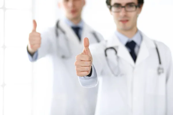 Zwei männliche Ärzte stehen als Team und zeigen Daumen nach oben als Symbol für den besten Service für Patienten in der Klinik. Medizin und Gesundheitsfürsorge — Stockfoto