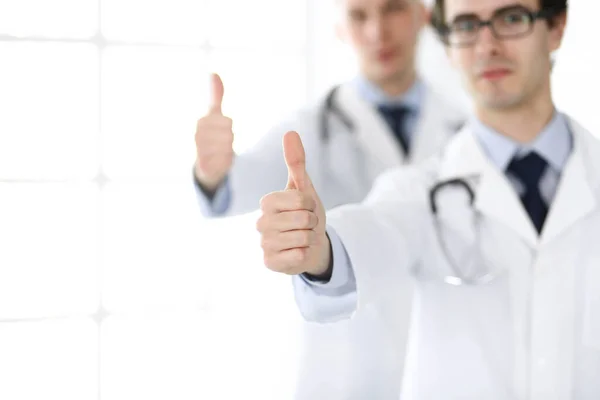 Two male doctors standing as a team and showing thumbs up as a symbol of the best service for patients in the clinic. Medicine and health care — Stock Photo, Image