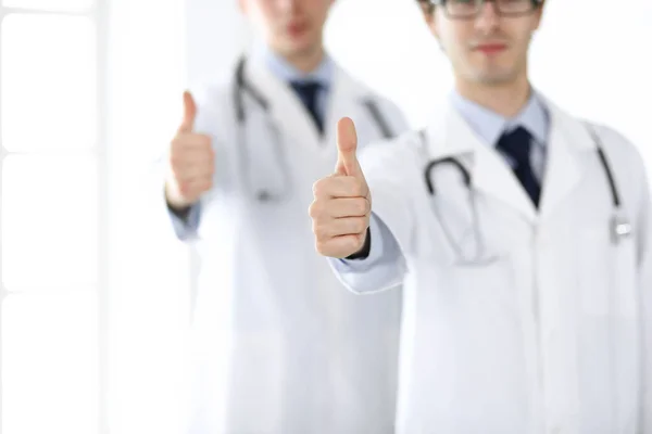 Twee mannelijke artsen staan als een team en tonen duimen omhoog als een symbool van de beste service voor patiënten in de kliniek. Geneeskunde en gezondheidszorg — Stockfoto