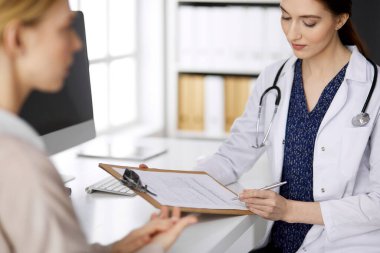 Dost canlısı gülümseyen kadın doktor ve hasta kadın klinikte otururken sağlık muayenesini tartışıyorlar. Hastanede mükemmel bir tıbbi hizmet. Tıp konsepti