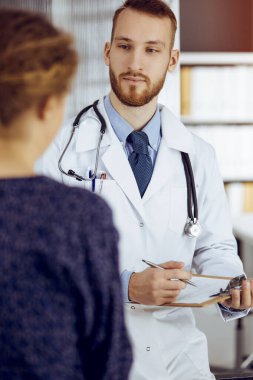 Dost canlısı sakallı doktor ve hasta kadın güneşli klinikte otururken sağlık muayenesini tartışıyorlar. Tıp konsepti