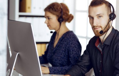 Modern güneşli ofiste otururken kulaklıkla konuşan sakallı iş adamı. Çağrı merkezinde çeşitli insanlar grubu