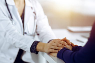 Bilinmeyen kadın-doktor, klinikteki güneşli dolapta otururken güncel sağlık muayenesini tartışarak hastalarının ellerini tutuyor. Steteskoplu bir doktor iş başında.