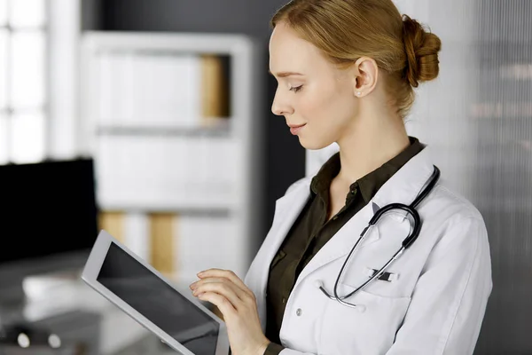 Friendly smiling female doctor using clipboard in clinic. Portrait of friendly physician woman at work place. Perfect medical service in hospital — Stock Photo, Image