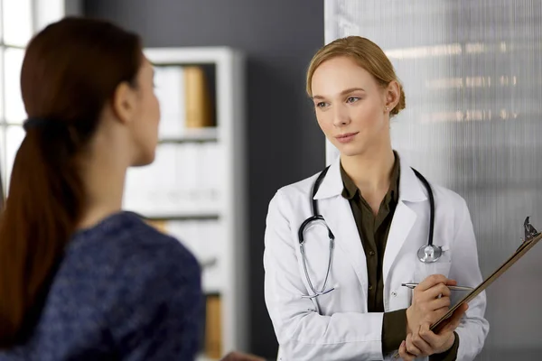 Femme souriante amicale médecin et patiente discutant de l'examen de santé en cours alors qu'elle était assise à la clinique. Service médical parfait à l'hôpital. Concept de médecine — Photo