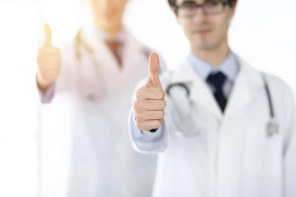 Twee mannelijke artsen staan als een team en tonen duimen omhoog als een symbool van de beste service voor patiënten in zonnige kliniek. Geneesmiddelenconcept — Stockfoto