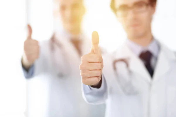 한 팀으로 서 있는 두 명의 남성 의사들 이 양지바른 병원의 환자들을 위한 최고의 서비스의 상징으로 엄지손가락을 보여 주고 있습니다. 의학적 개념 — 스톡 사진