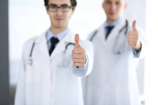Двоє чоловіків-лікарів стоять в команді і показують великі пальці як символ найкращої служби для пацієнтів у клініці. Медицина та охорона здоров'я — стокове фото