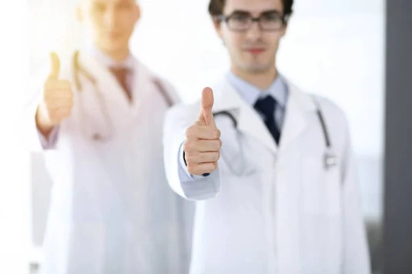 Twee mannelijke artsen staan als een team en tonen duimen omhoog als een symbool van de beste service voor patiënten in zonnige kliniek. Geneesmiddelenconcept — Stockfoto
