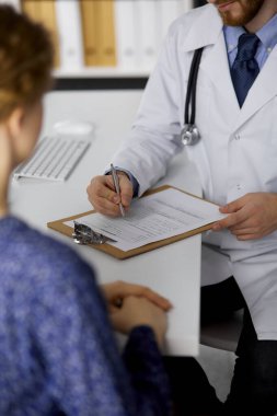 Bilinmeyen sakallı doktor ve hasta kadın güneşli klinikte otururken sağlık muayenesini tartışıyorlar. Yakın plan. Tıp konsepti