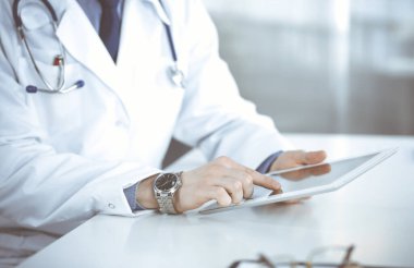 Bilinmeyen erkek doktor klinikteki tablet bilgisayarla yakın planda çalışıyor. İşteki genç doktor. Mükemmel sağlık hizmeti, tıp konsepti