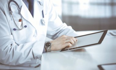 Bilinmeyen erkek doktor klinikteki tablet bilgisayarla yakın planda çalışıyor. İşteki genç doktor. Mükemmel sağlık hizmeti, tıp konsepti