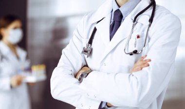 Koruyucu maskeli kimliği belirsiz erkek doktor klinikte kollarını kavuşturmuş duruyor. Coronavirus salgını sırasında ilaç konsepti. Covid 2019