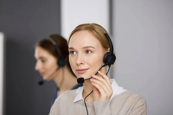 Barátságos üzletasszony fülhallgatóval beszél, miközben az irodában ül. Call center és változatos emberek csoport az üzleti életben — Stock Fotó