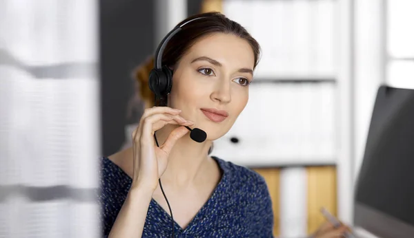 Ázsiai vagy latin-amerikai üzletasszony fülhallgatóval beszél, miközben hivatalban van. Call center és változatos emberek csoport az üzleti életben — Stock Fotó
